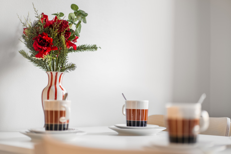 Mesa de comedor blanca con tres tazas y un arreglo de flores rojas