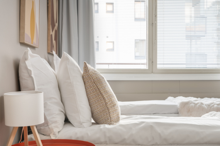 Cama blanca junto a una ventana amplia con persianas