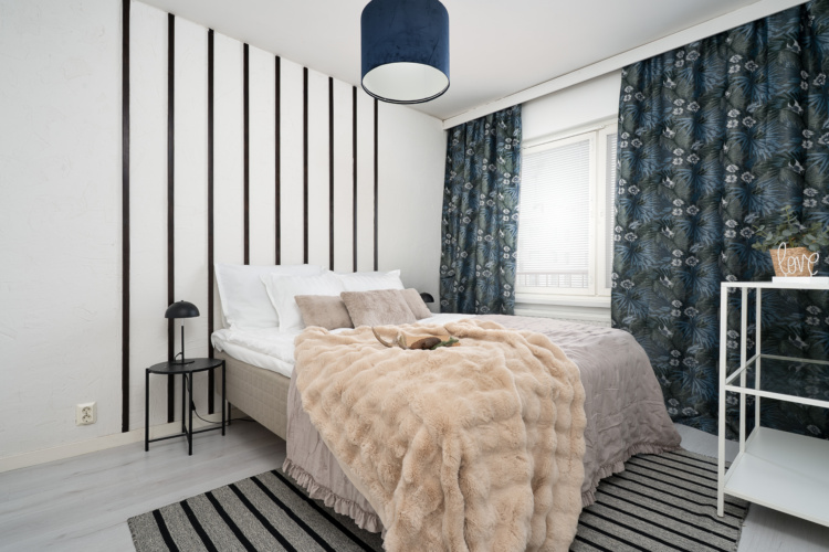 Dormitorio blanco y negro con pared de paneles, cortinas estampadas y colcha beige