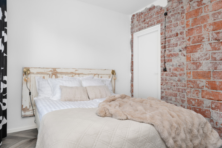 Dormitorio blanco con pared de ladrillo visto y cama con estructura de latón