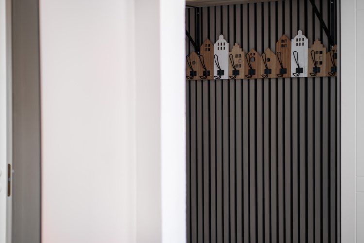 Percheros con forma de casas montados en una pared oscura de listones verticales