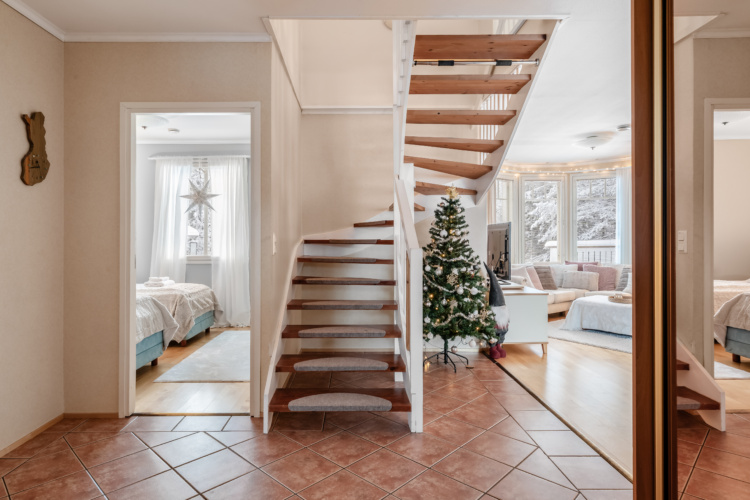 Vestíbulo con una escalera abierta de madera que conduce a una sala decorada para Navidad