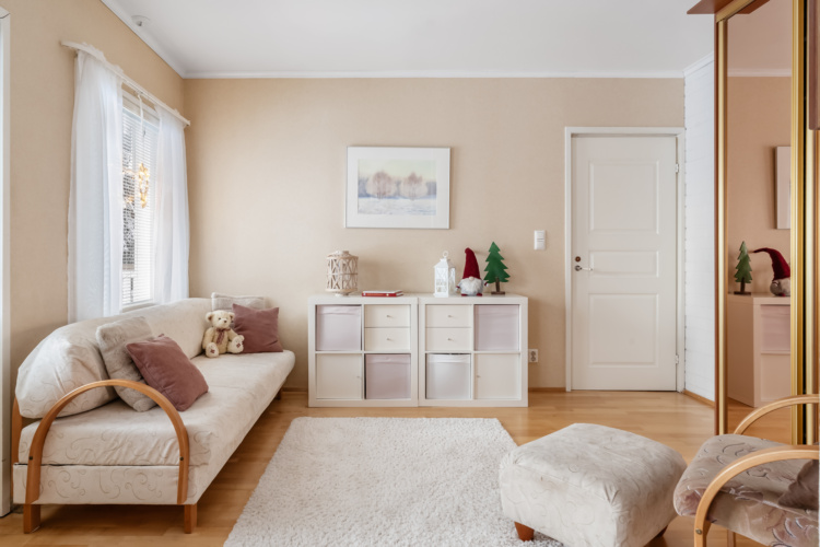 Pequeña sala con sofá color crema, mueble de almacenaje y puerta blanca cerrada