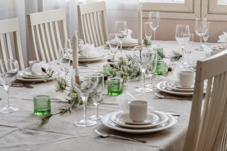 Mesa puesta con vajilla blanca, copas, velas y adornos verdes festivos