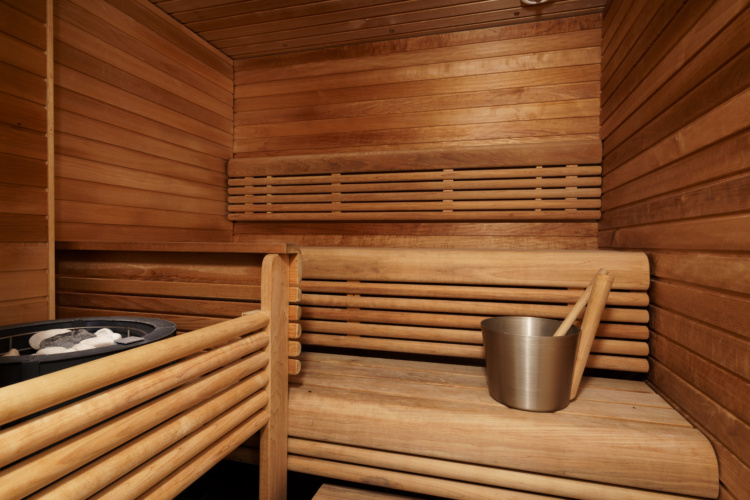 Sauna revestida de madera con bancos escalonados, piedras del calentador y cubo metálico
