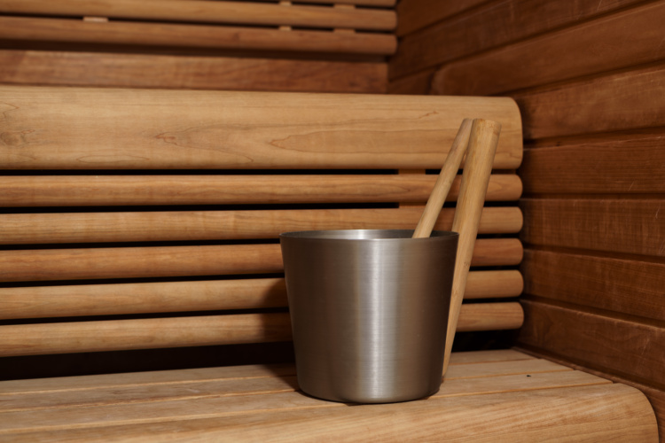 Cubo metálico de sauna y cucharón sobre un banco de madera