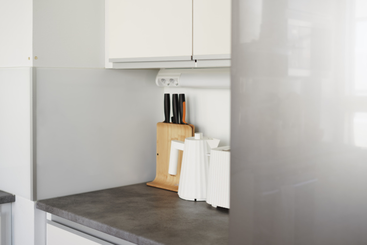 Rincón de cocina blanco con encimera oscura, bloque de cuchillos y portarrollos de papel