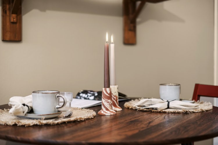 Mesa redonda puesta para dos con tazas de cerámica, individuales tejidos y una vela encendida