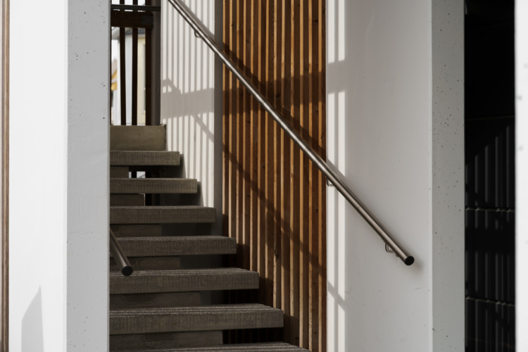 Escalera de hormigón junto a listones verticales de madera y pasamanos de acero