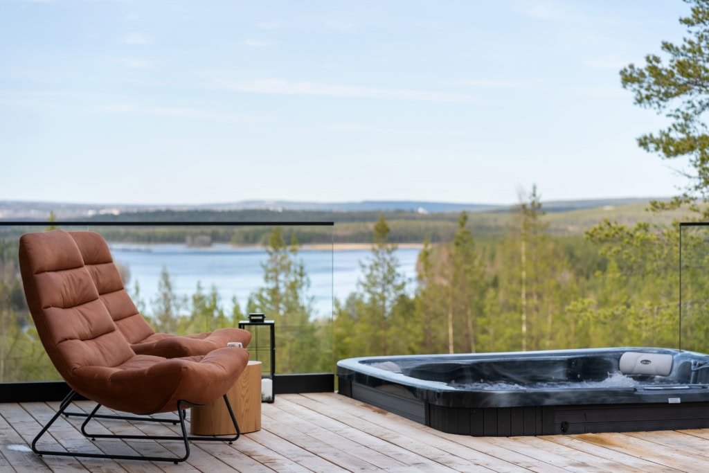 Terraza de una casa vacacional en Laponia: sillón y jacuzzi con vistas al lago y al bosque
