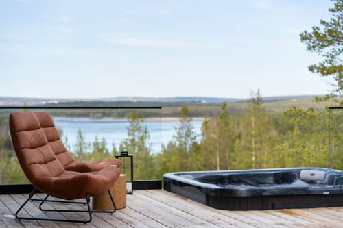 Terraza de una casa vacacional en Laponia: sillón y jacuzzi con vistas al lago y al bosque