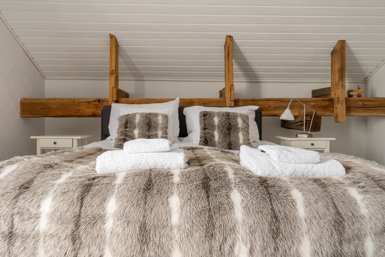Cama de dormitorio con manta y cojines de pelo bajo antiguas vigas de madera