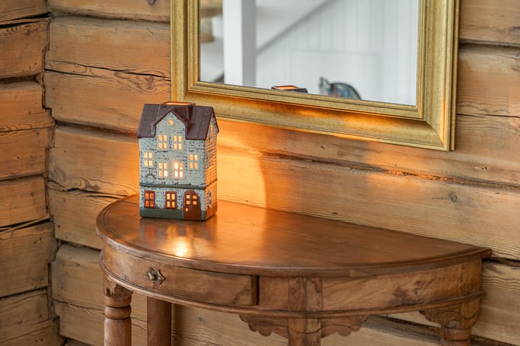 Casita de cerámica iluminada por una vela sobre una mesa antigua ante una pared de troncos