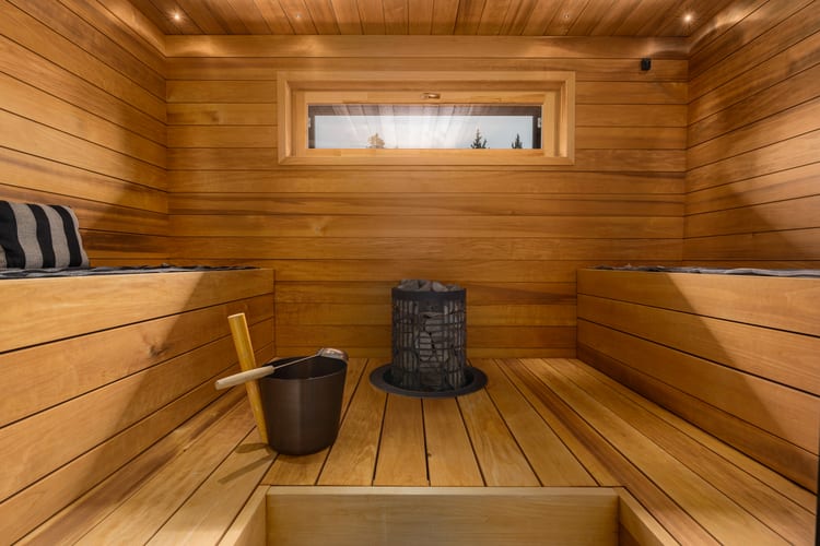 Sauna, jossa musta kiuas, puinen kiulu ja lauteiden yläpuolella kapea ikkuna