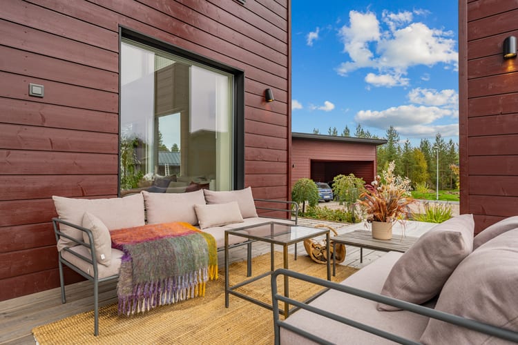 Terassin sohvaryhmä punaista puuseinää vasten, värikäs villa syysauringossa