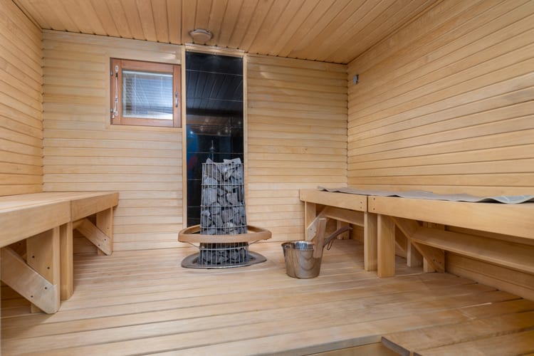 Vaalea sauna, jossa leveät lauteet ja kiuas ikkunan vieressä